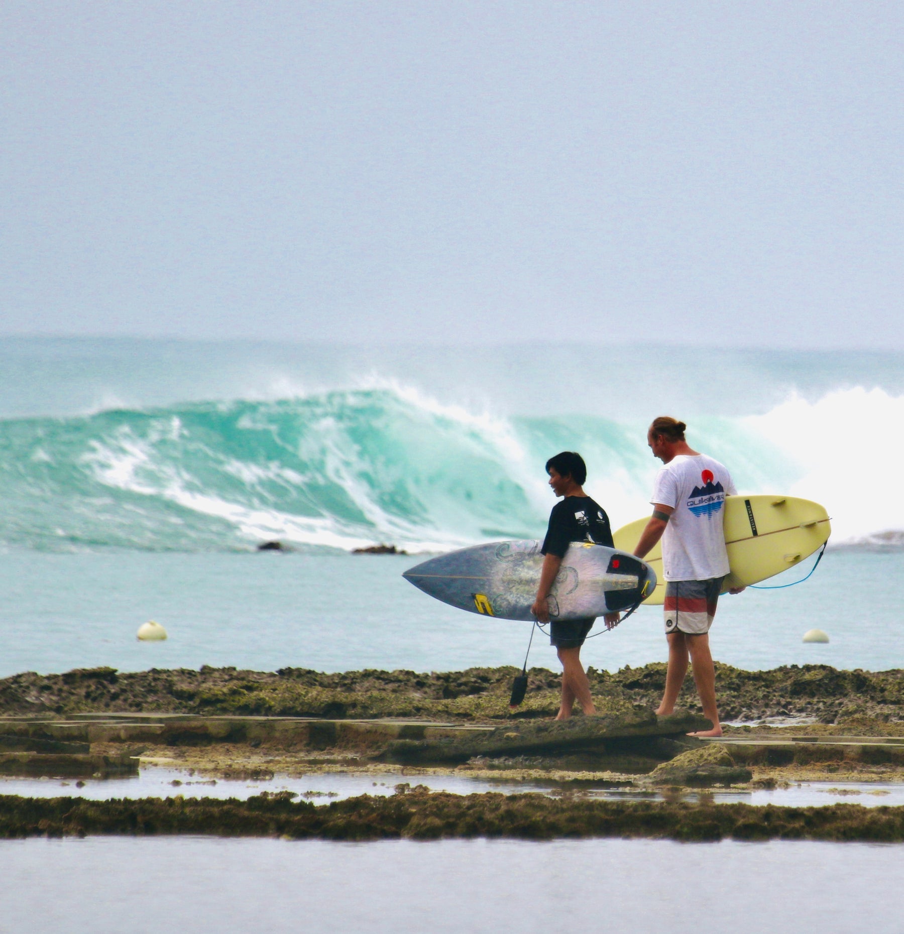 zwei surfer laufen mit surfboards in der hand zum Rifbreak Surfspot. im hintergrund brechen die Wellen des Meeres