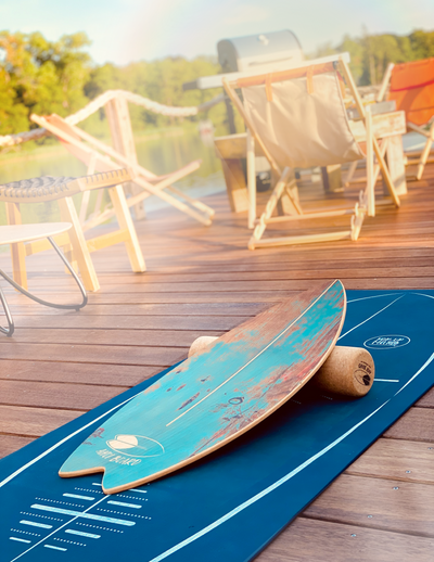 Türkises Balance Board liegt auf Korkrolle und blauer Matte im Hintergrund Holzterasse und sommerliche Atmosphäre